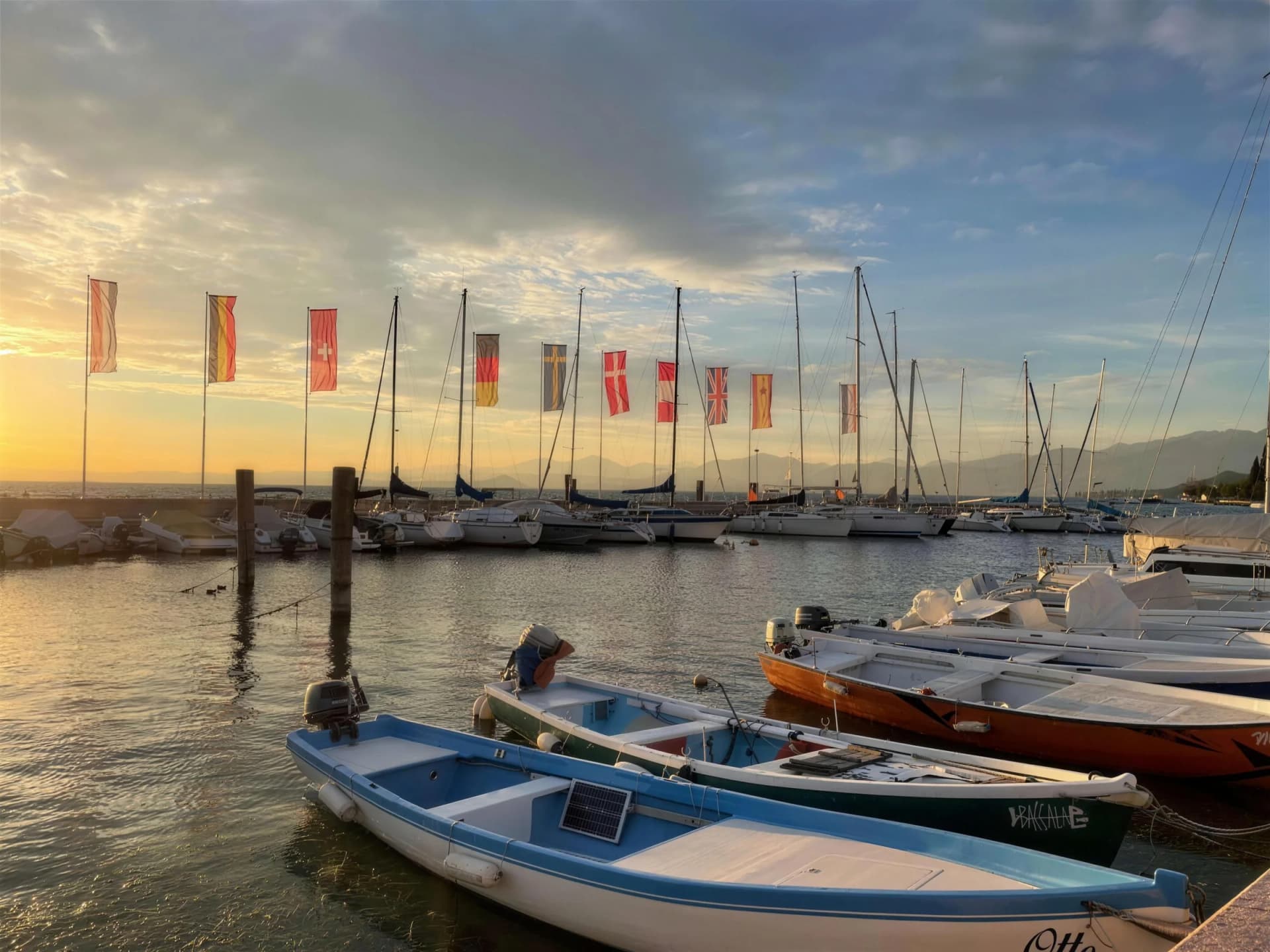 Kleiner Hafen mit Ruderbooten, Segelbooten und Fahnen bei Sonnenuntergang